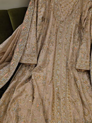 A close-up of an ornate beige or taupe traditional garment with extensive gold, silver, and pastel embroidered detailing, draped to show the fabric texture and pattern.